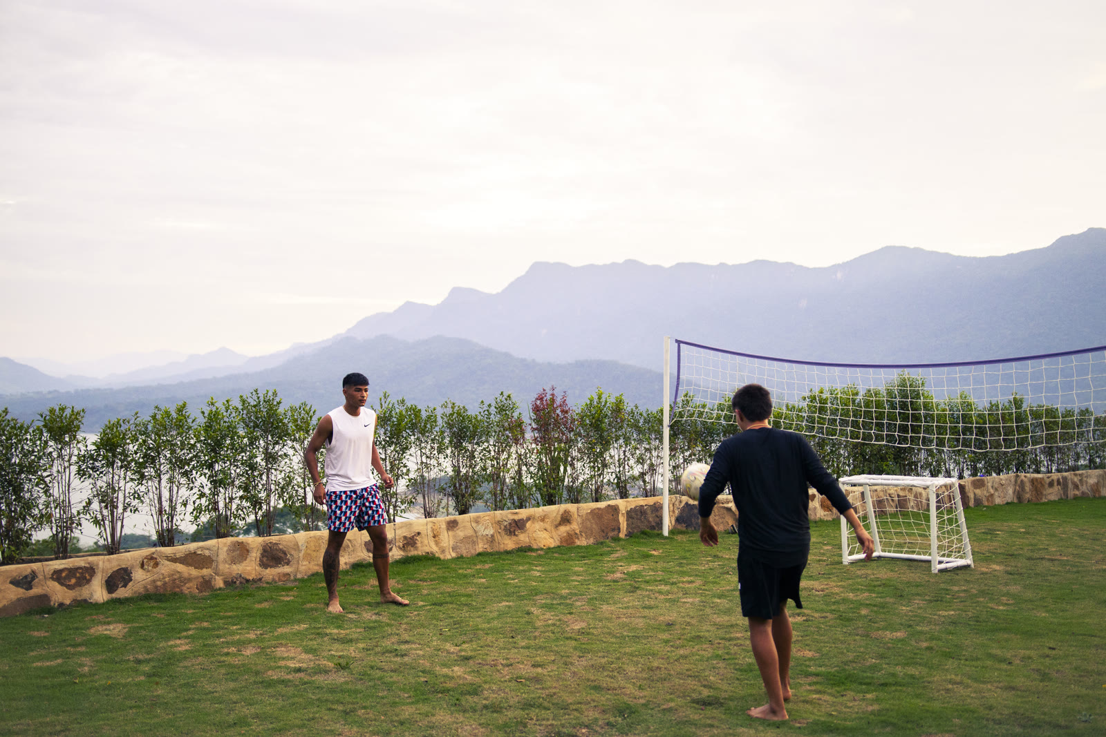 Dos amigos jugando fútbol al atardecer en Altos de Yariguíes, con el Embalse de Topocoro y las montañas al fondo