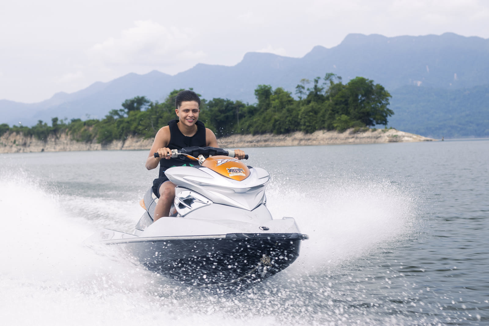 A young man rides a jet ski and throws up a wake on the Topocoro Reservoir, with green mountains behind him