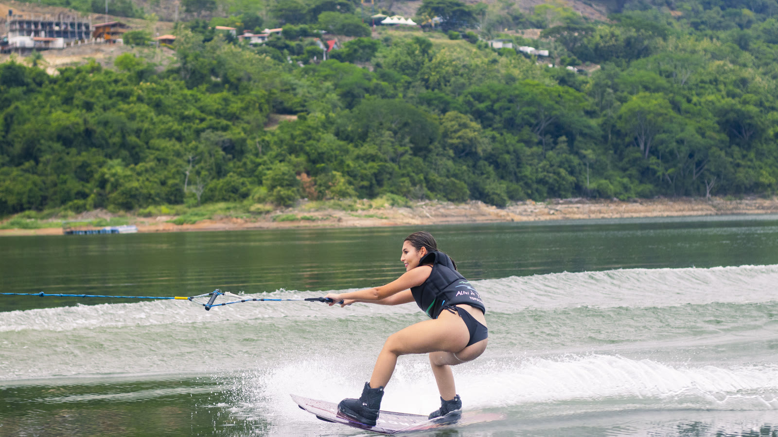 A woman wakeboards on the Topocoro Reservoir with a green hillside in the background